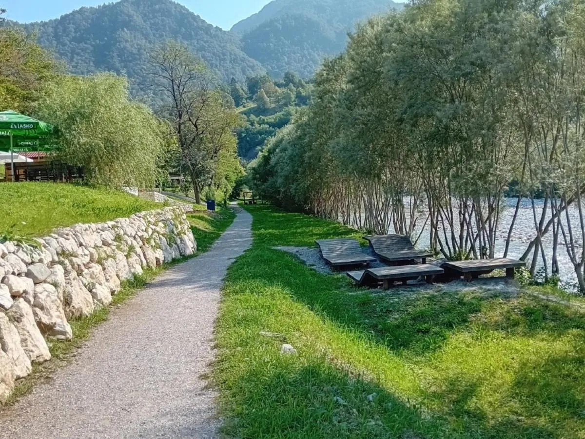 Pot ob reki, kamnit zid in leseni ležalniki na travi