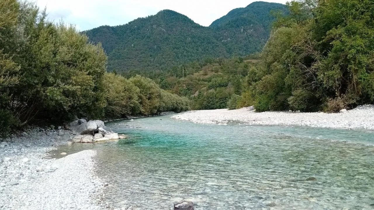 Turkizna Tolminka s prodnatim bregom, za njo gozdnati hribi
